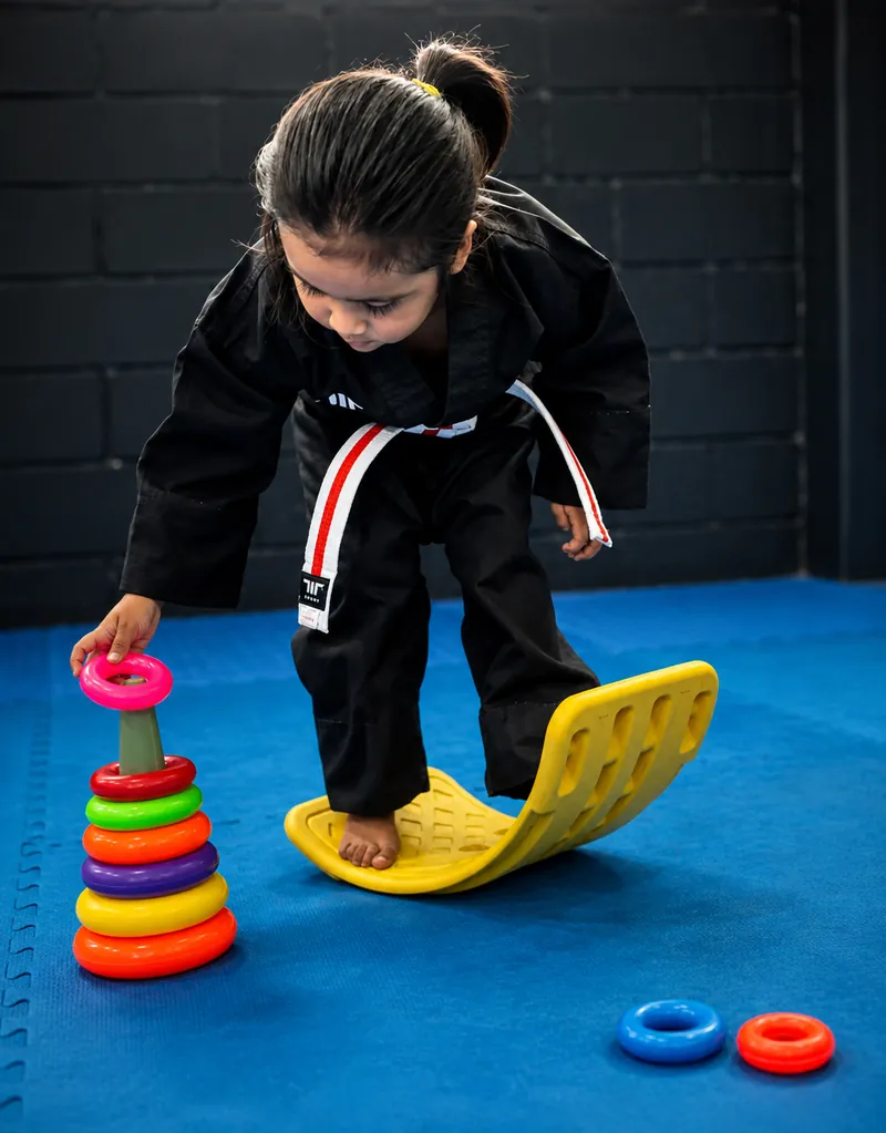 Niña pequeña trabajando equilibrio y psicomotricidad sobre una tabla con aros de colores en clase de Taekwondo.