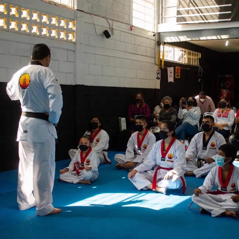 Instructor de Kyeongju dirigiendo a un grupo de alumnos sentados en el tatami del dojang mientras las familias observan.