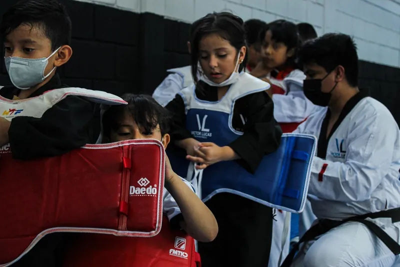 Niñas y niños colocándose petos de protección antes de una práctica de combate en clase de Taekwondo.